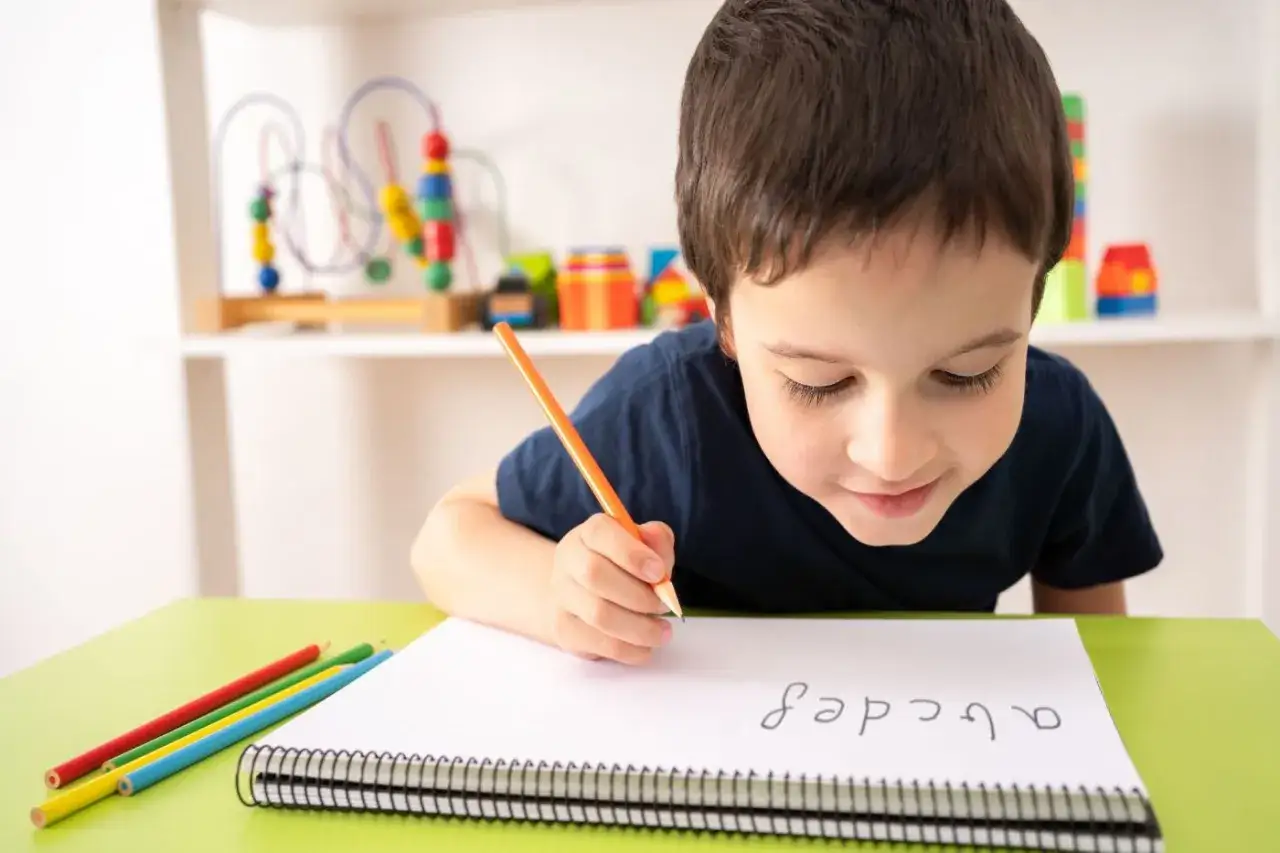 Niño concentrado practicando el texto primaria en su cuaderno con lápices de colores.