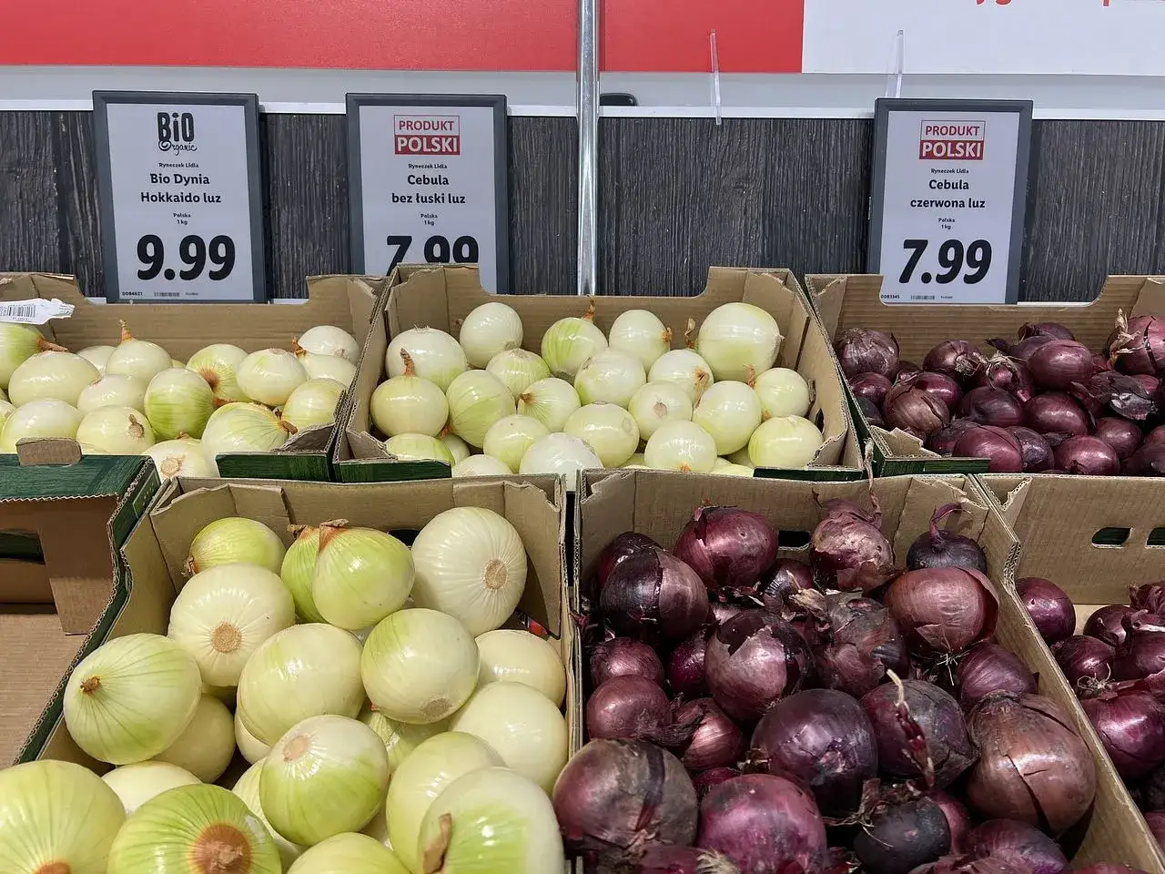 Cebula biała i czerwona w kartonach, polskie produkty. Cena białej cebuli 7.00, czerwonej 7.99.