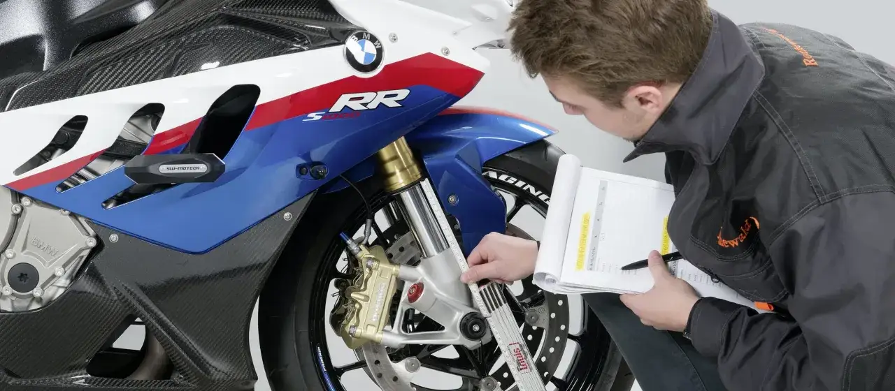 Mechanik sprawdza geometrię motocykla BMW S1000RR, mierząc zawieszenie i notując dane.