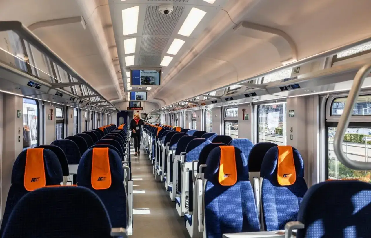 Wnętrze nowoczesnego pociągu PKP Intercity. Puste, niebieskie fotele z pomarańczowymi zagłówkami czekają na pasażerów. eic co to za pociąg?