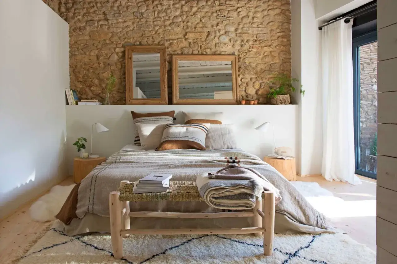 Ideas como decorar una habitación de matrimonio moderna: cama con textiles cálidos, pared de piedra rústica, espejos de madera y alfombra acogedora.
