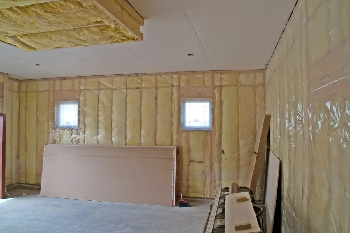 Travaux en cours pour isoler le garage. L'isolant jaune est visible sur les murs et le plafond, avec des plaques de plâtre prêtes à être posées.