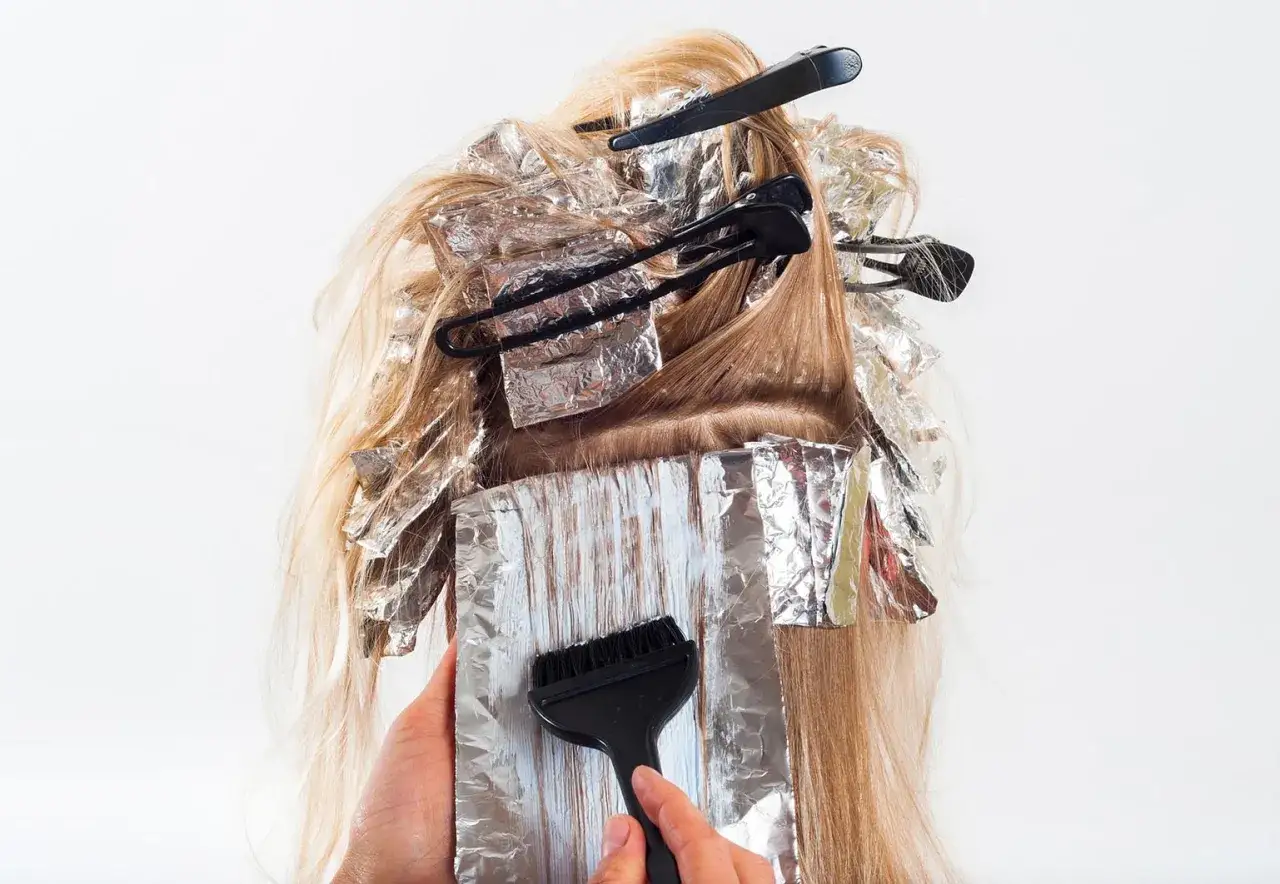 H&aring;rstylist applicerar f&auml;rg med pensel p&aring; slingor i blont h&aring;r, inlindade i folie. En blivande mamma som vill fr&auml;scha upp sitt h&aring;r.