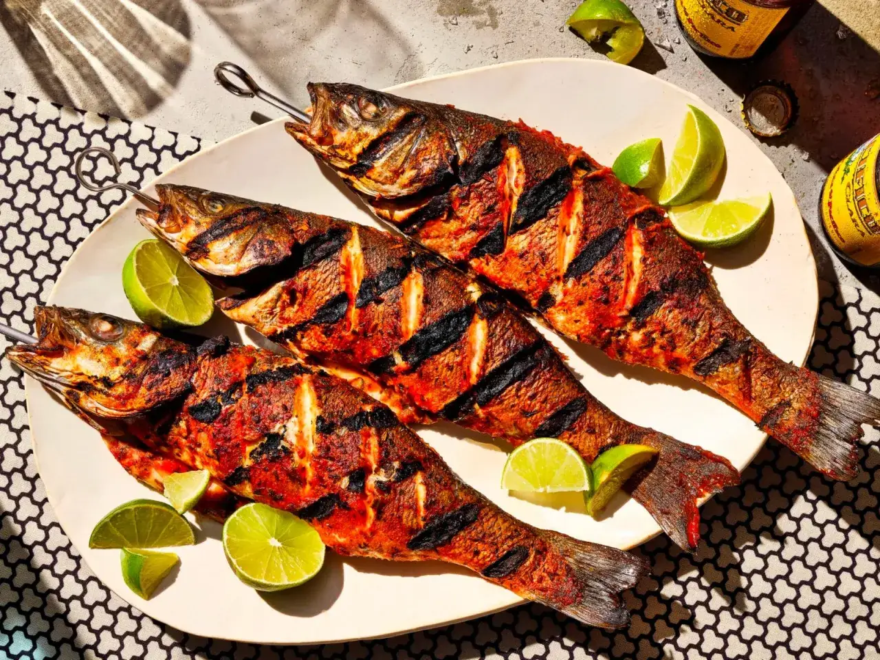 Tre pesci interi, cotti alla perfezione su una griglia, adornano un piatto con spicchi di lime. Una deliziosa grigliata di pesce pronta da gustare.