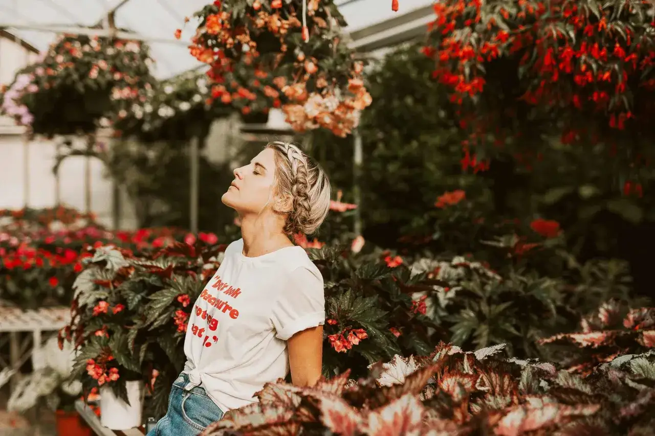 Frau genie&szlig;t den Tag im Gew&auml;chshaus, umgeben von Blumen. Ihr T-Shirt sagt: 