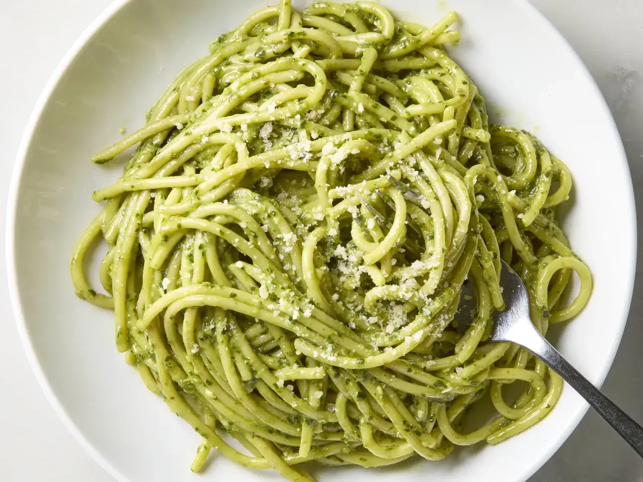 Pyszny makaron z pesto, posypany parmezanem, czeka na widelcu w białej misce.