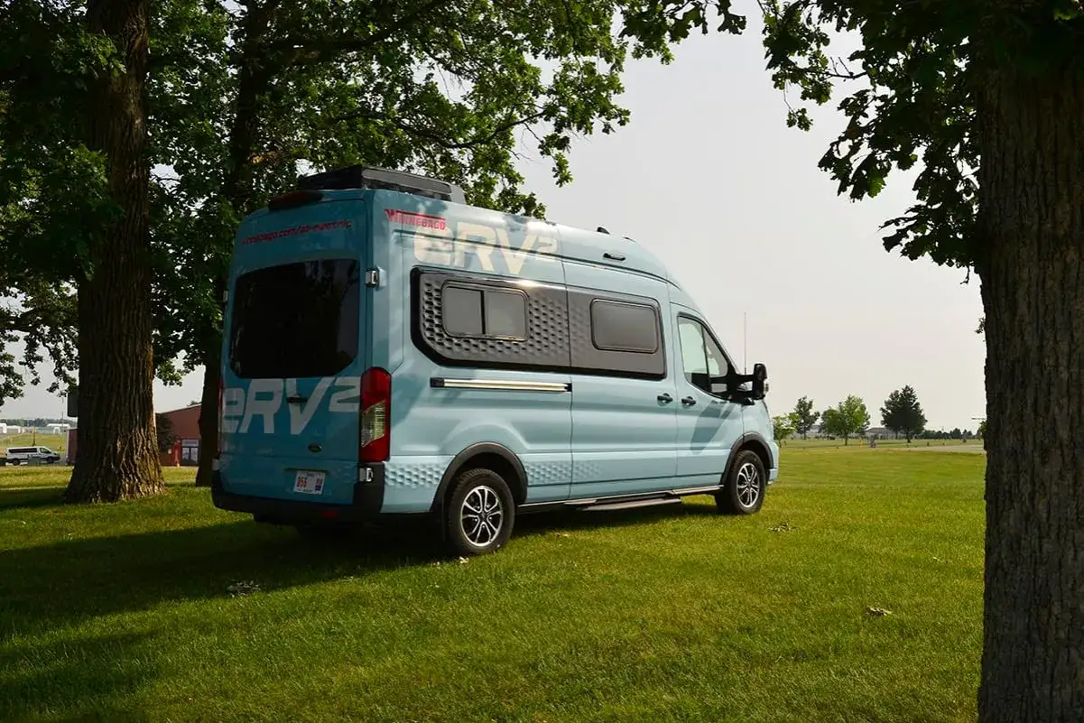 En ljusblå eldriven plåtis, en Winnebago ERV2, står parkerad på en gräsmatta under träd.