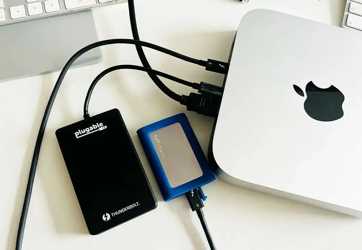 Externe Festplatten sind angeschlossen, um den **MacBook Speicher erweitern**. Ein Mac Mini mit Apple Logo ist zu sehen.