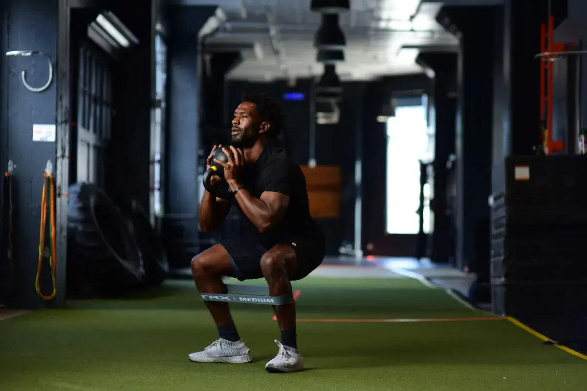 Mann macht Kniebeugen mit Kettlebell und Widerstandsband für starke Kettlebell Beine.