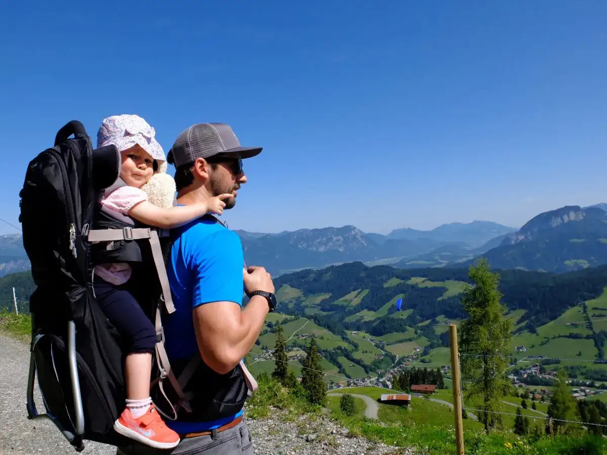 Ein Mann tr&auml;gt ein Kind in einer Kraxe auf einem Berg. Die Kraxe ist ein praktisches Hilfsmittel f&uuml;r Wanderungen mit Kleinkindern.