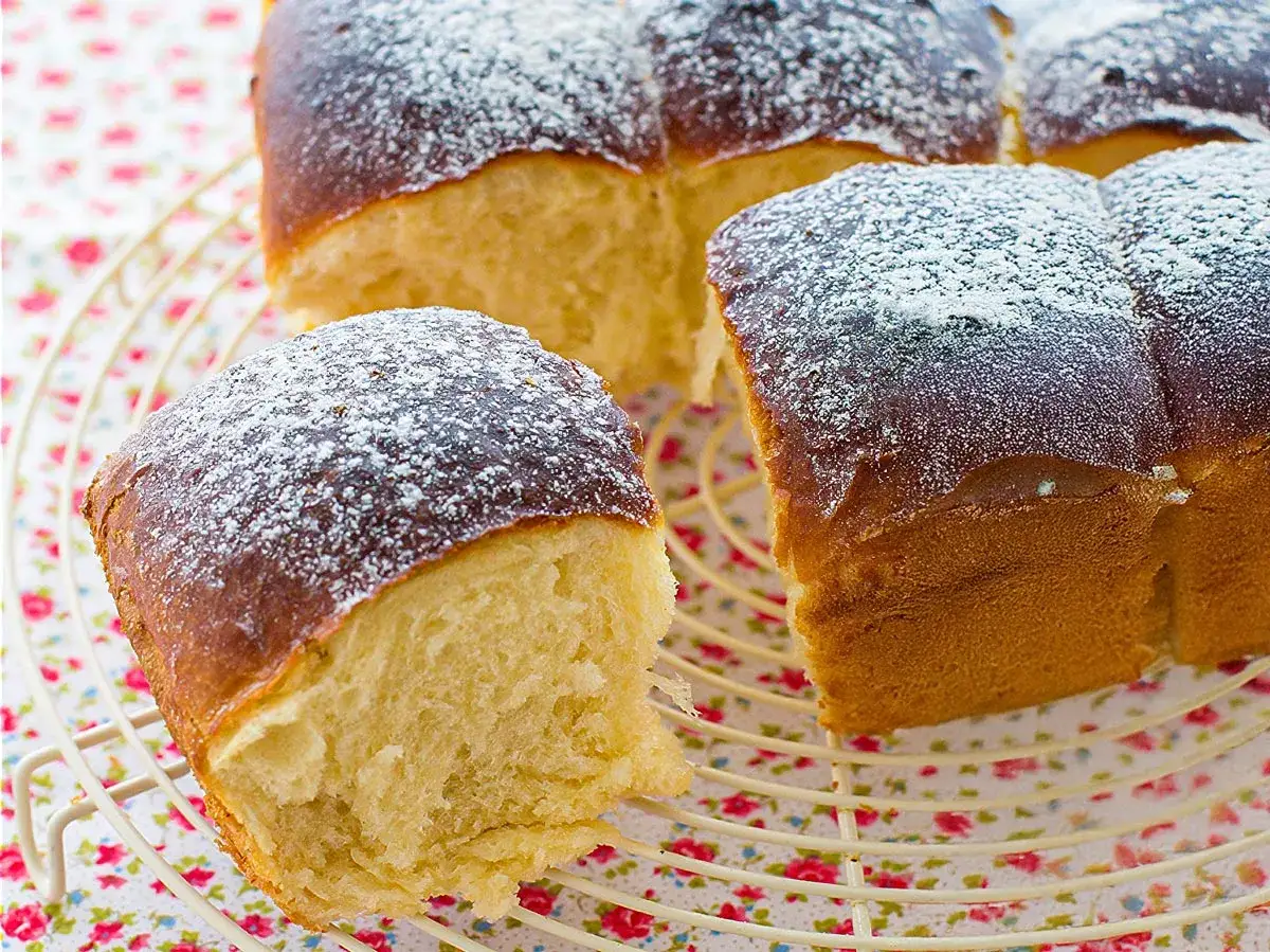 Pan de brioche esponjoso y dorado, espolvoreado con azúcar glas sobre una rejilla.