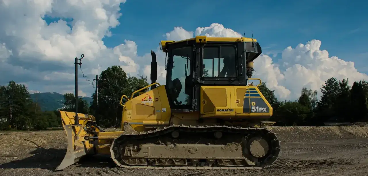 Żółta spycharka Komatsu D51PX czeka na kurs na spycharki. W tle góry i chmury.