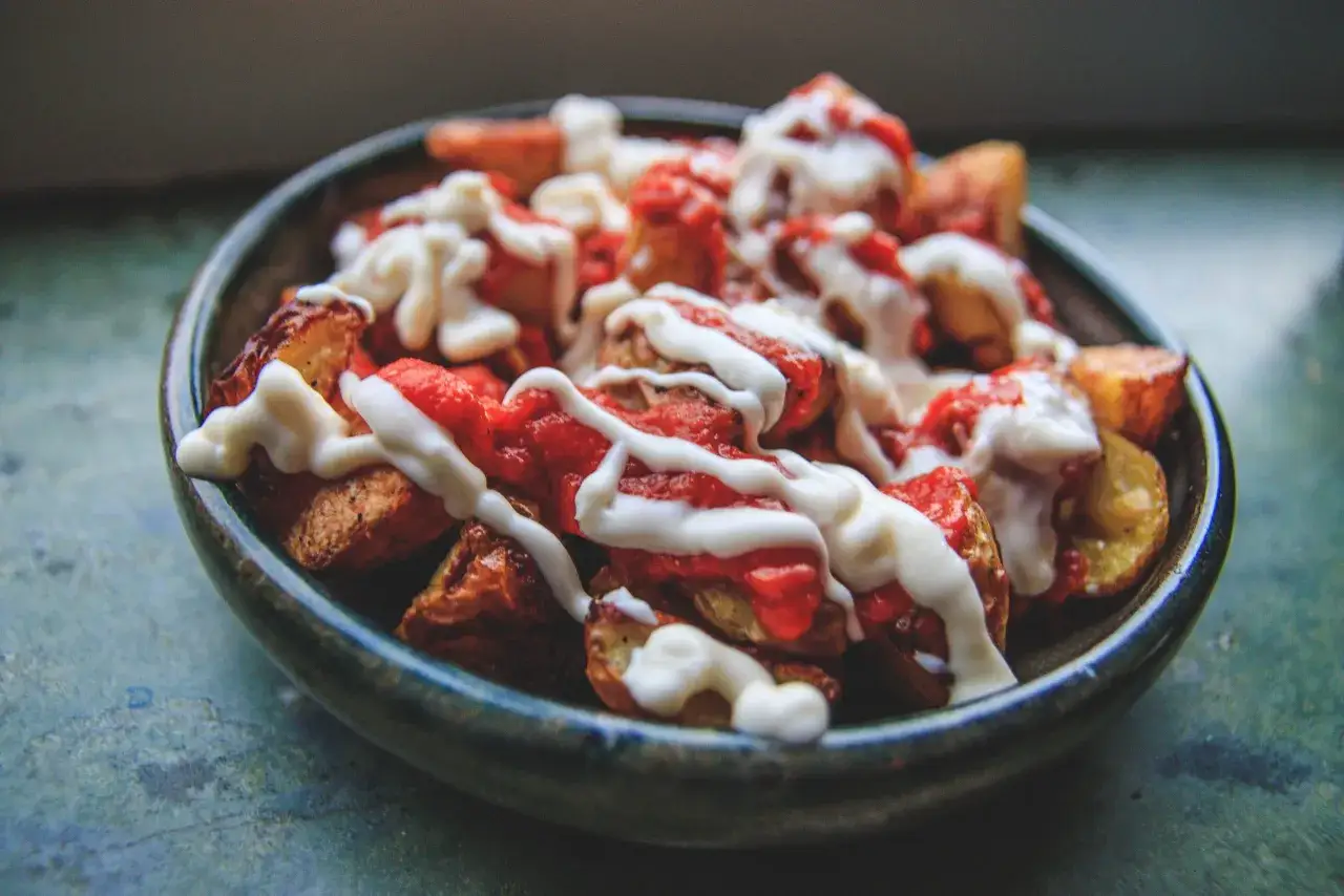 En skål med krispiga tater tots, toppade med röd sås och en krämig dressing.