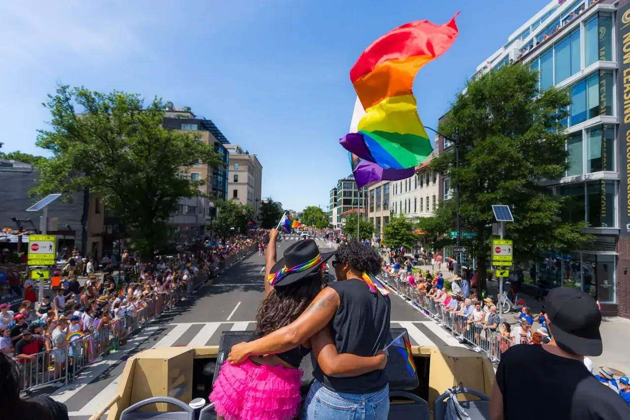 Two people embrace on a float, holding a rainbow flag at a Pride parade, a celebration found in many of the most gay cities in the US.