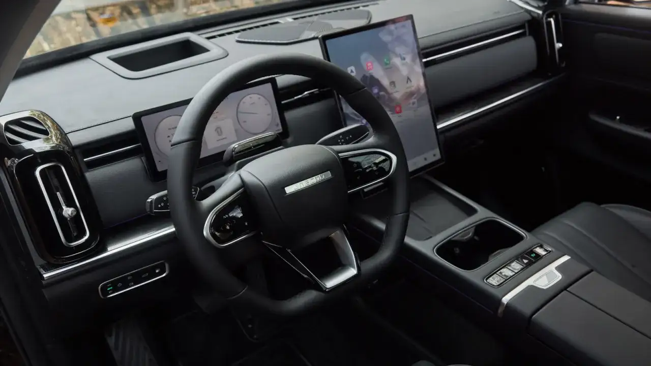 Wnętrze nowoczesnego samochodu Jaecoo 7 Super Hybrid z dużym ekranem dotykowym i cyfrowymi zegarami.