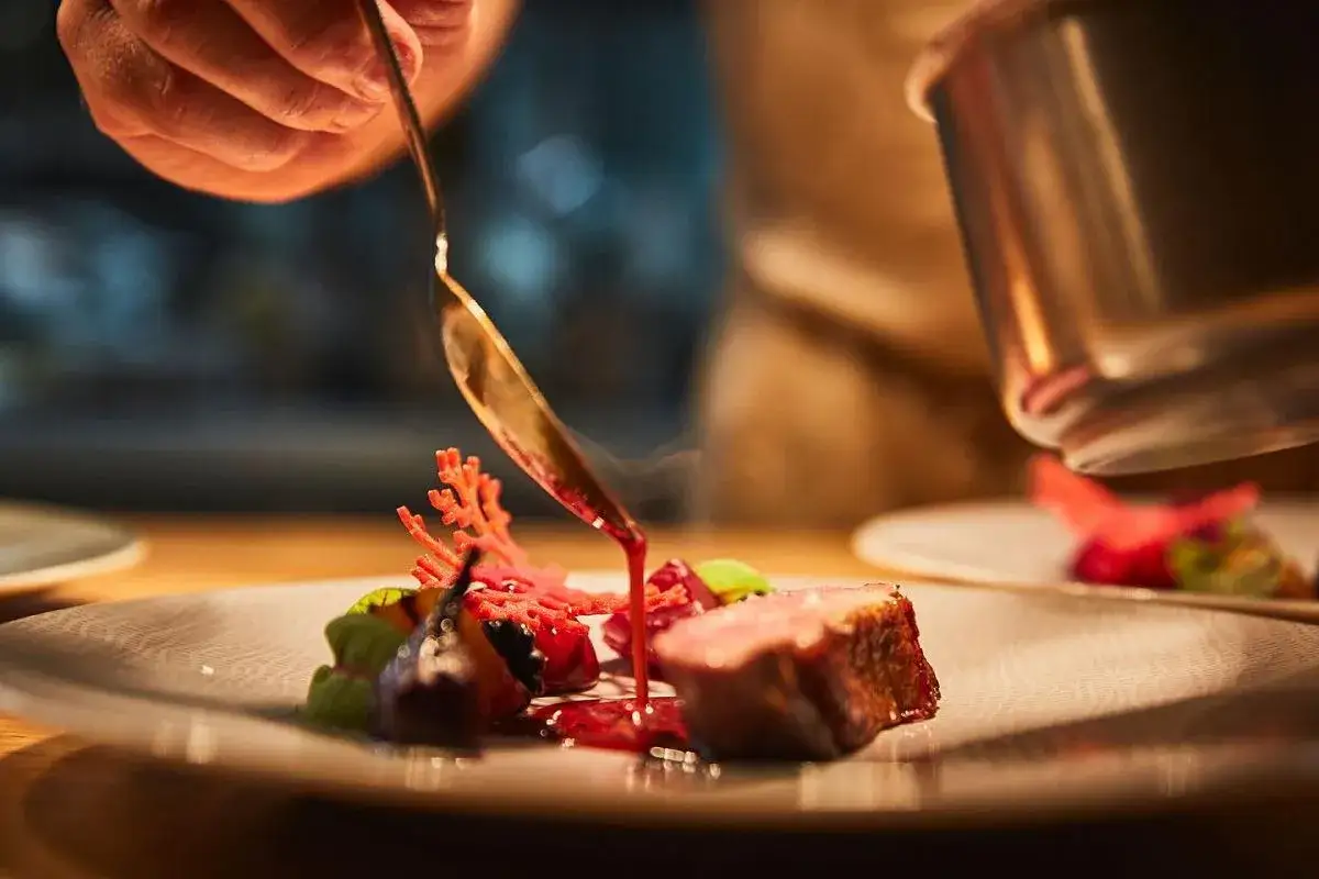 Szef kuchni w restauracji z gwiazdką Michelin precyzyjnie polewa danie sosem.