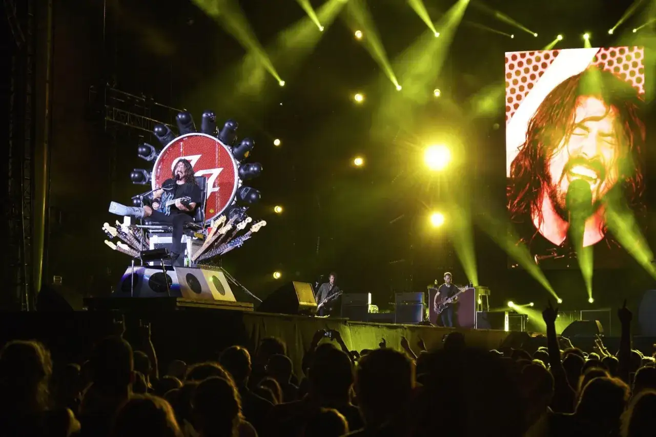 Dave Grohl z zespołem na scenie, otoczony światłami i ekranami. Tłum szaleje.