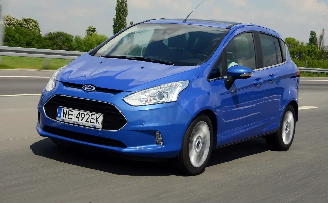 Niebieski Ford B-Max pędzi po autostradzie, jego sylwetka odbija się w słońcu.