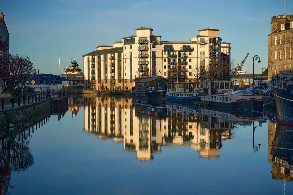 Edificios modernos y barcos reflejados en el agua tranquila del puerto de Leith, Edimburgo.