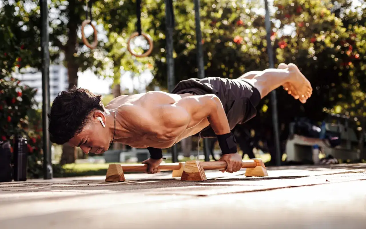 Un athl&egrave;te en plein exercice de calisthenics militaire, effectuant des pompes sur barres parall&egrave;les en ext&eacute;rieur.