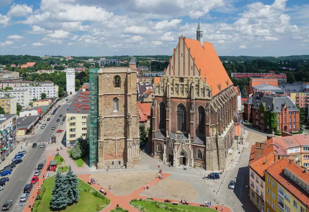 Nysa trasa widok na zabytkowy kości&oacute;ł i wieżę wodną, z ulicą pełną samochod&oacute;w i zielenią miejską.