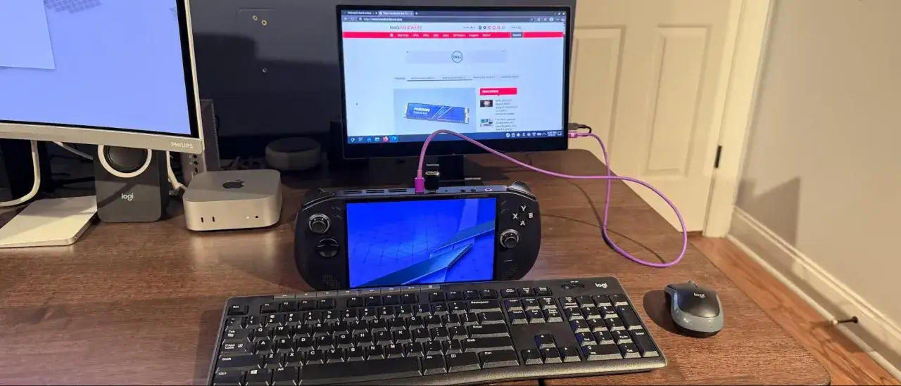 Dispositivo portátil con pantalla azul conectado a un monitor, teclado y ratón. Parece un PC con Steam OS listo para jugar.