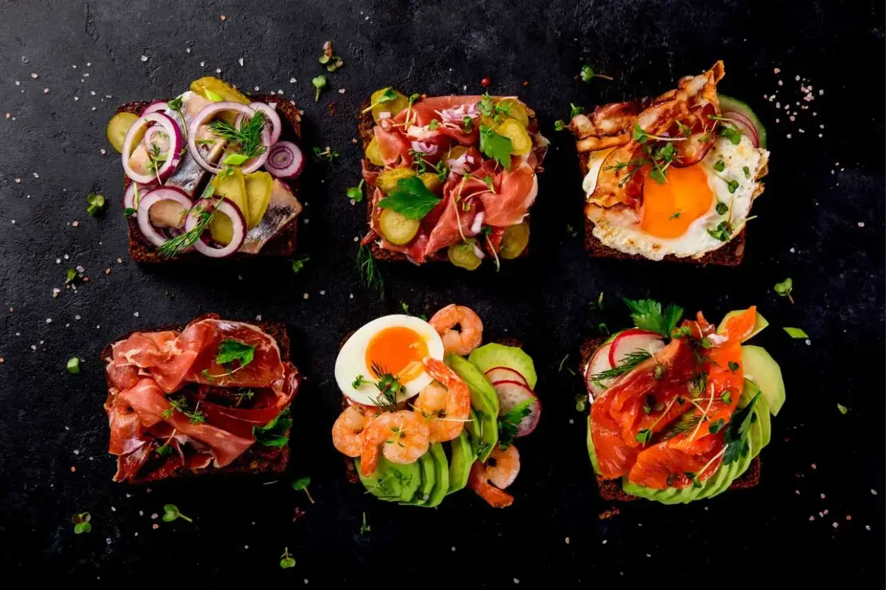 Sex olika varma mackor i ugn med olika pålägg: sill, prosciutto, ägg med bacon, räkor med avokado och lax med avokado.