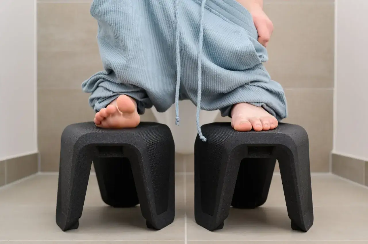 F&uuml;&szlig;e auf Hockern, um den **stuhlgang nach geburt** zu erleichtern. Die Person sitzt auf der Toilette, die Hose heruntergezogen.