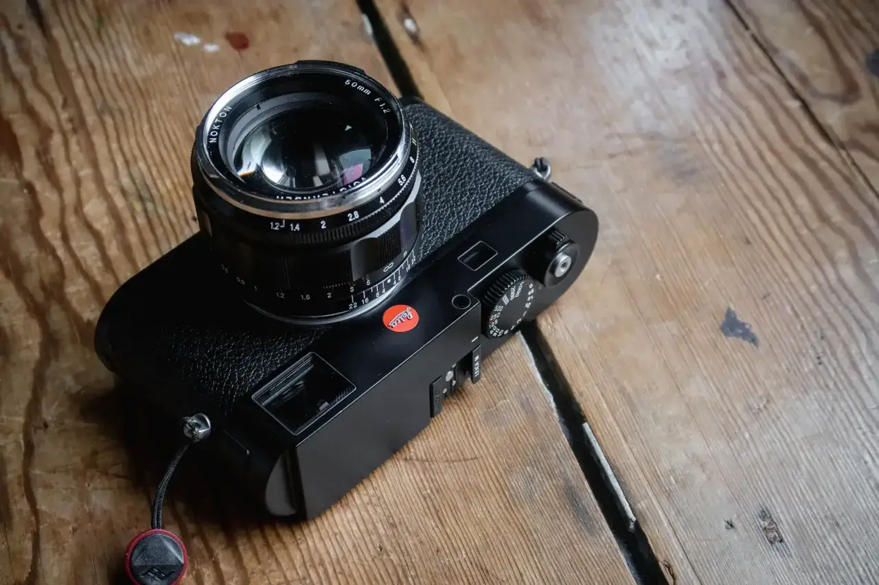 A black Leica M262 camera with a Nokton 50mm f/1.2 lens rests on a wooden surface.