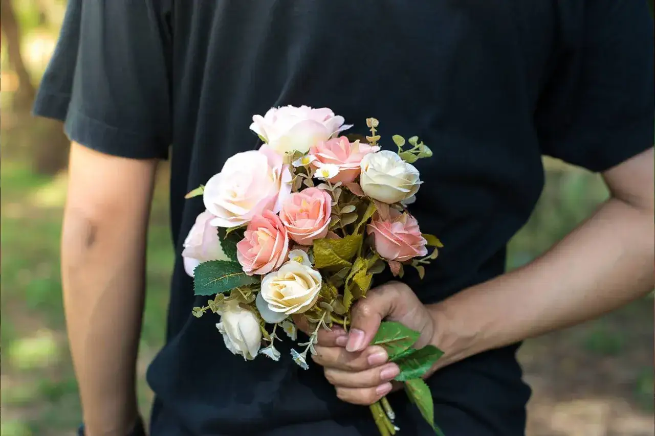 Un ramo de flores para pedir perd&oacute;n, con rosas en tonos rosa p&aacute;lido, melocot&oacute;n y blanco, oculto tras la espalda de una persona.