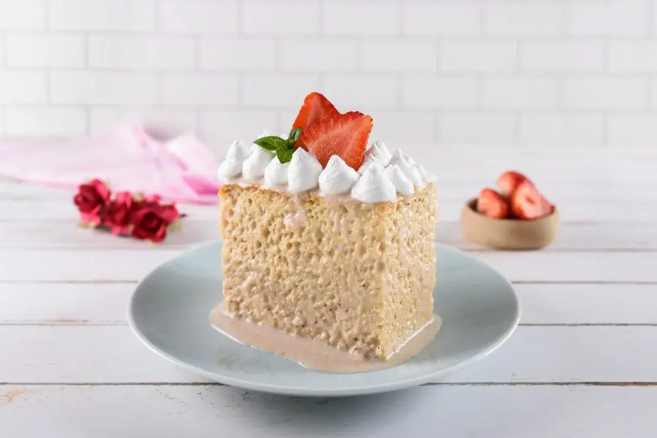 Un trozo de tarta tres leches, esponjoso y empapado en leche, coronado con merengue y fresas.