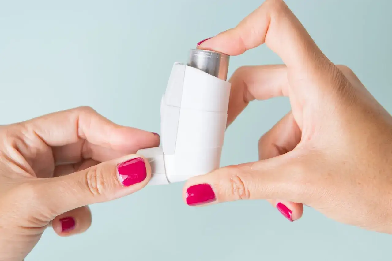 Dłonie z malowanymi na fuksję paznokciami trzymają inhalator. To pomoc w leczeniu astmy, jak oxodil combo.