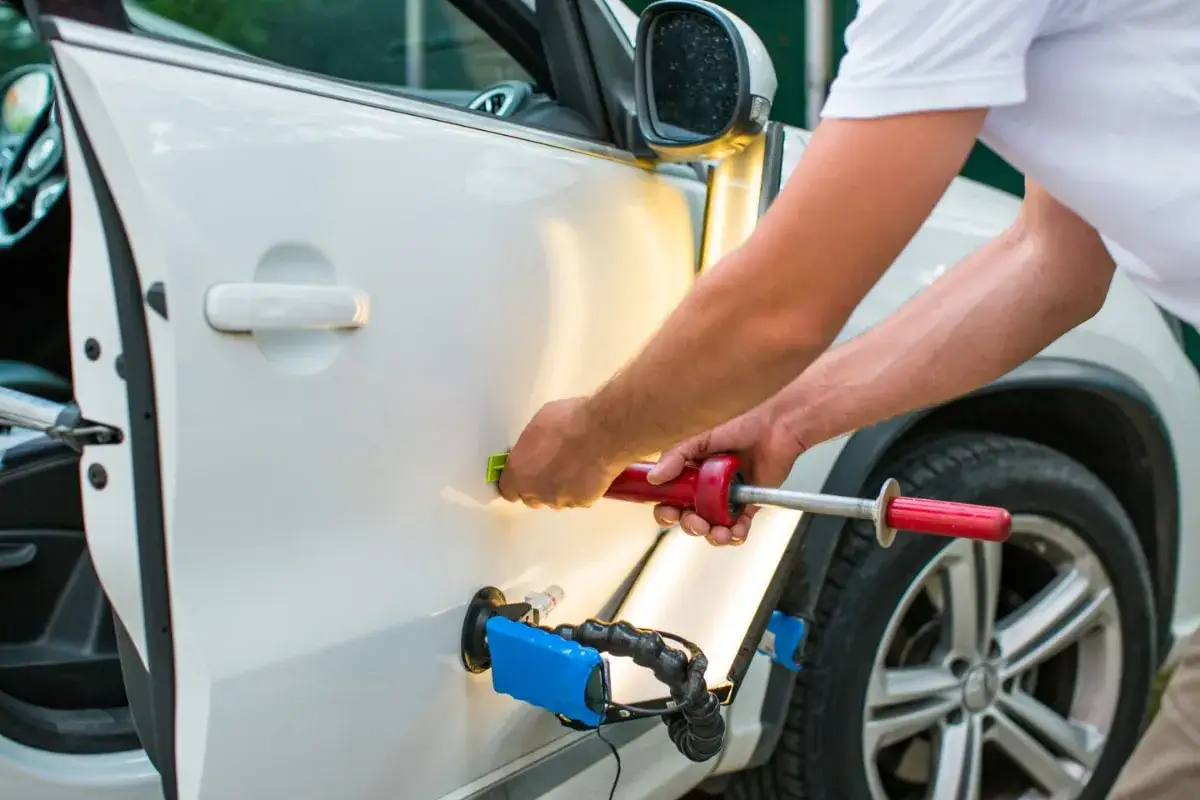 A technician uses a PDR tool to repair auto body damage on a white car door.