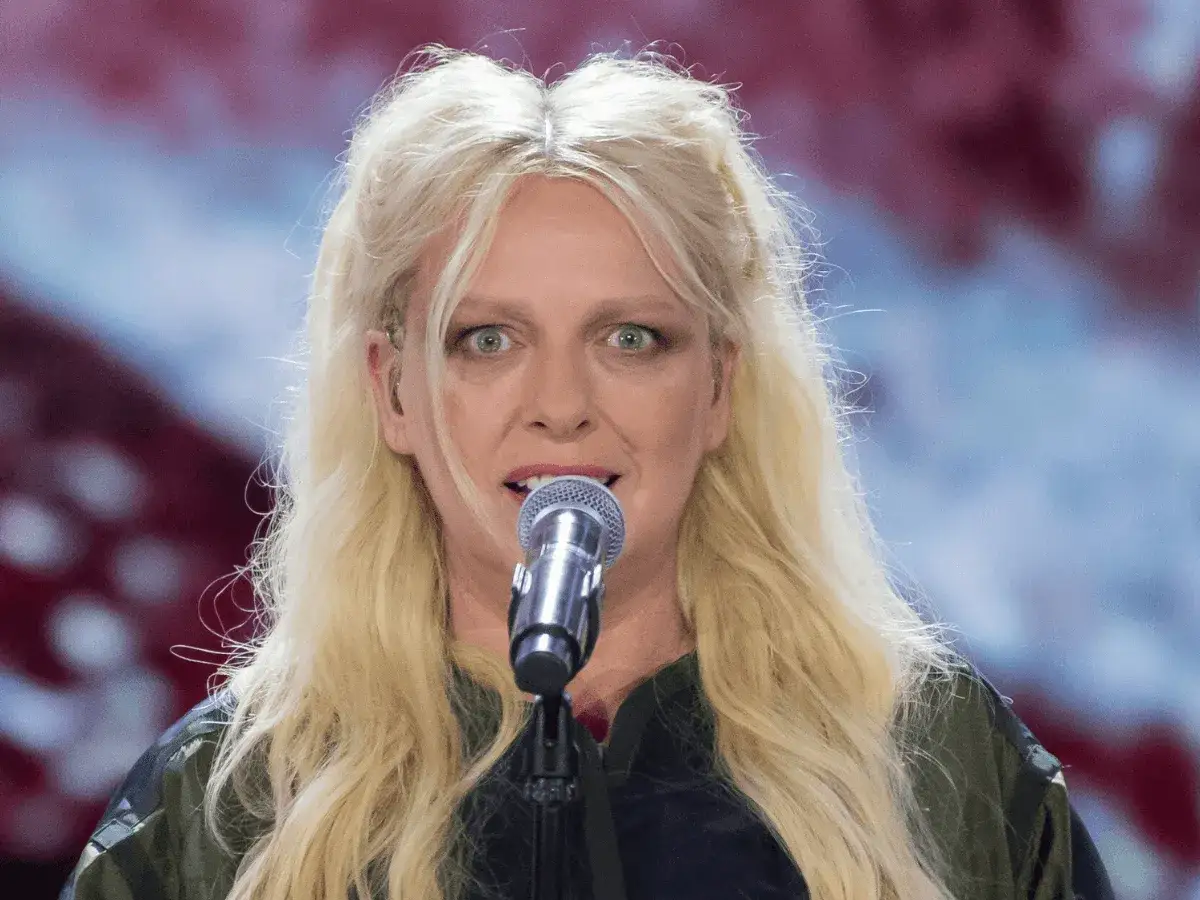 Ania Wyszkoni, wokalistka o blond włosach, śpiewa do mikrofonu. Jej wiek nie jest widoczny na zdjęciu, ale energia sceniczna jest wyczuwalna.