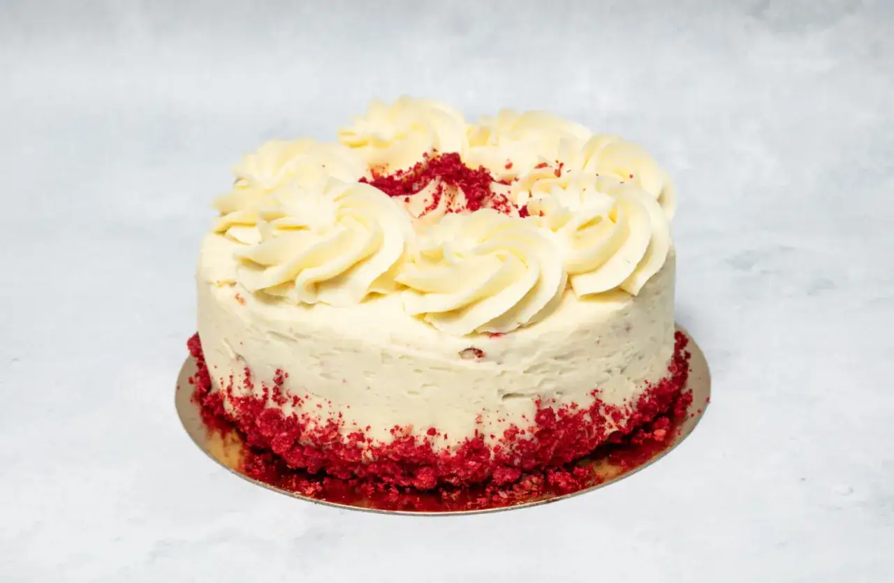 En vacker red velvet cake med kr&auml;mig frosting och r&ouml;da smulor runt kanten.