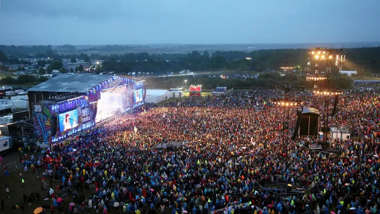 Tłum ludzi na koncercie, scena z ekranami, światła. To jest przystanek woodstock, niezapomniane chwile.