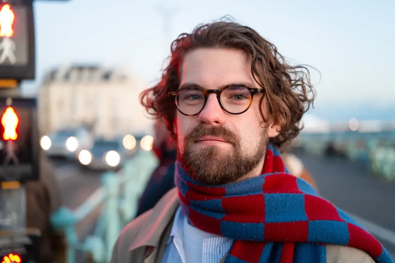 Un homme avec des lunettes et une écharpe à carreaux rouges et bleus, capturé lors d'un test du Leica Q3 dans un environnement urbain.
