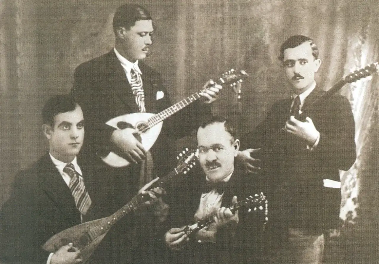 Quatre musiciens posent avec leurs instruments. L'un d'eux joue du bouzouki, un autre tient un instrument similaire.