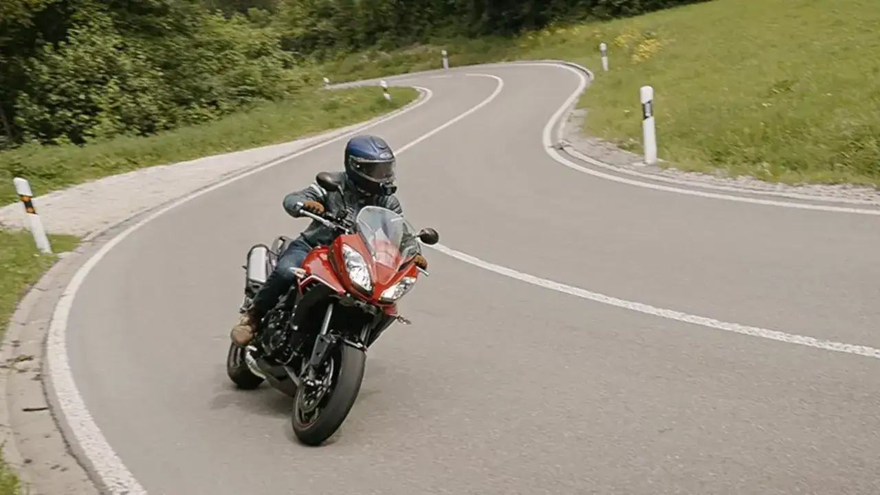 Motocyklista na czerwonym Triumph Tiger 1050 pokonuje zakręt na górskiej drodze. Dane techniczne tego modelu są imponujące.