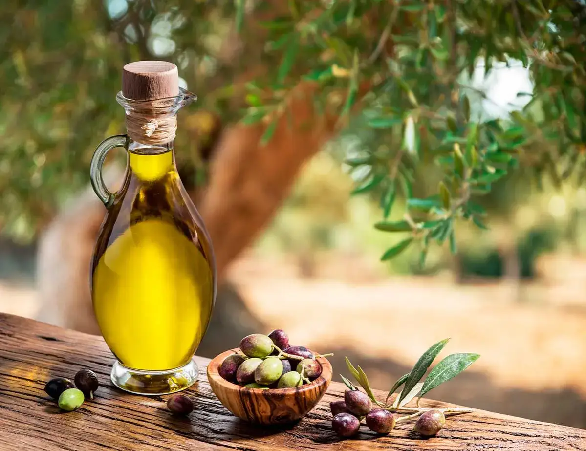 Aceite de oliva virgen en una jarra junto a aceitunas frescas en un cuenco, mostrando las diferencias entre oliva y aceituna.
