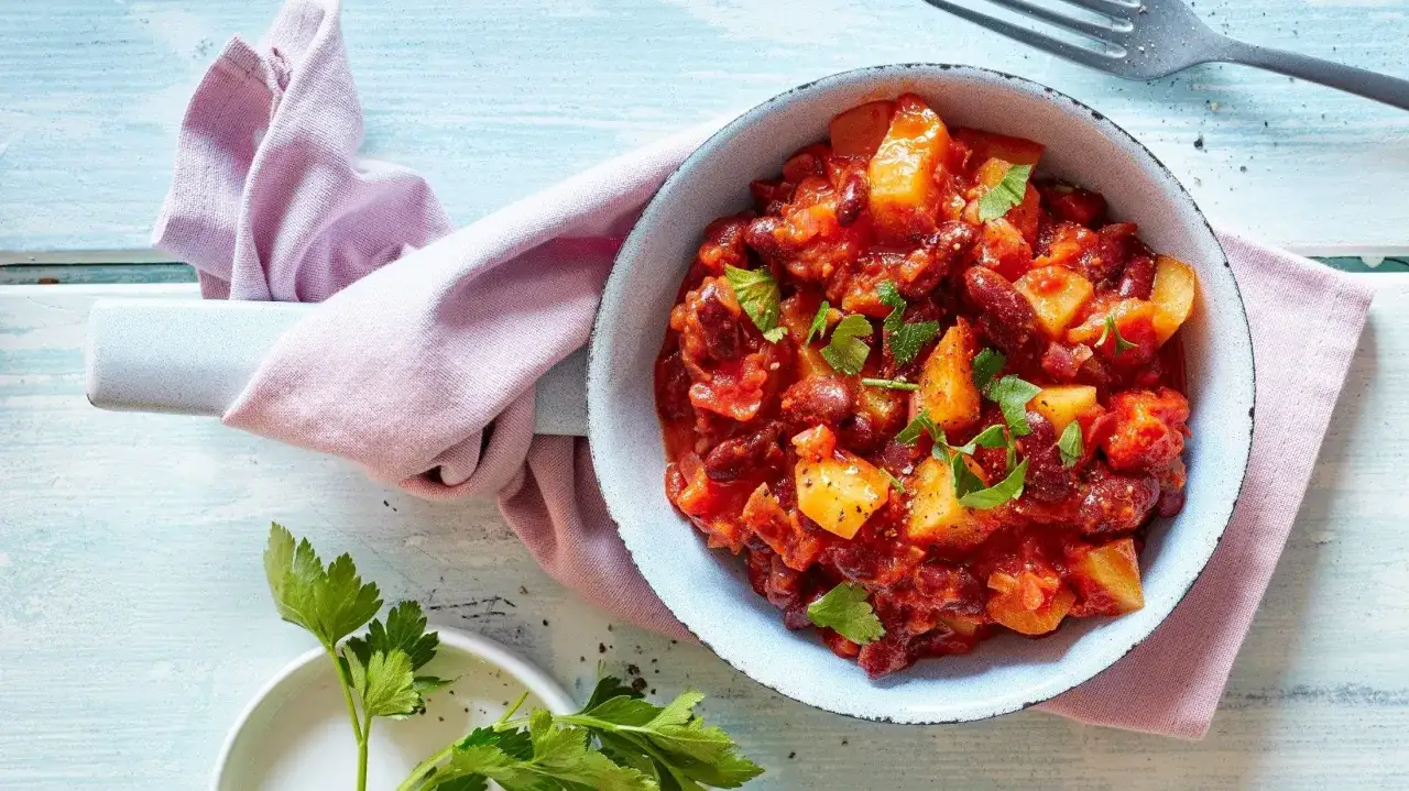 Herzhafte Kartoffel Bohnen Pfanne mit Tomaten und Petersilie, serviert in einer Schüssel auf einem hellblauen Holztisch.