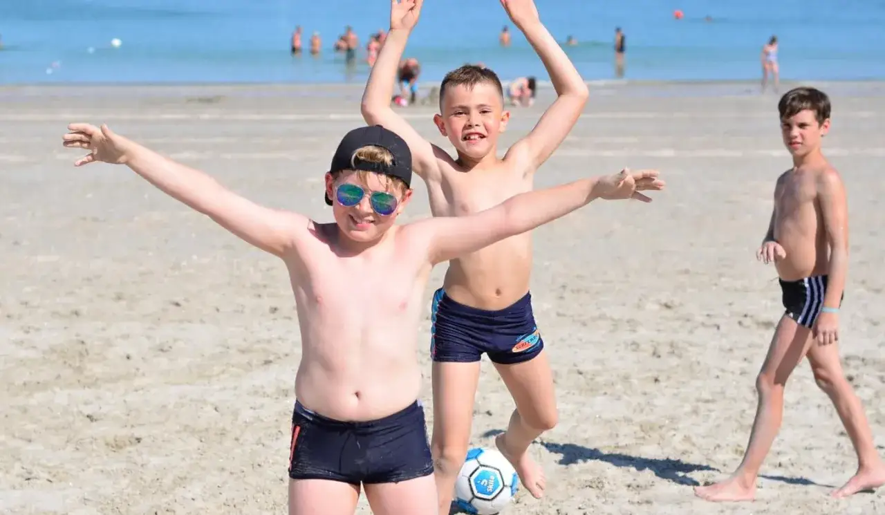 Trois garçons s'amusent sur la plage, un ballon de foot à leurs pieds. Un bel avis vacances pour tous !