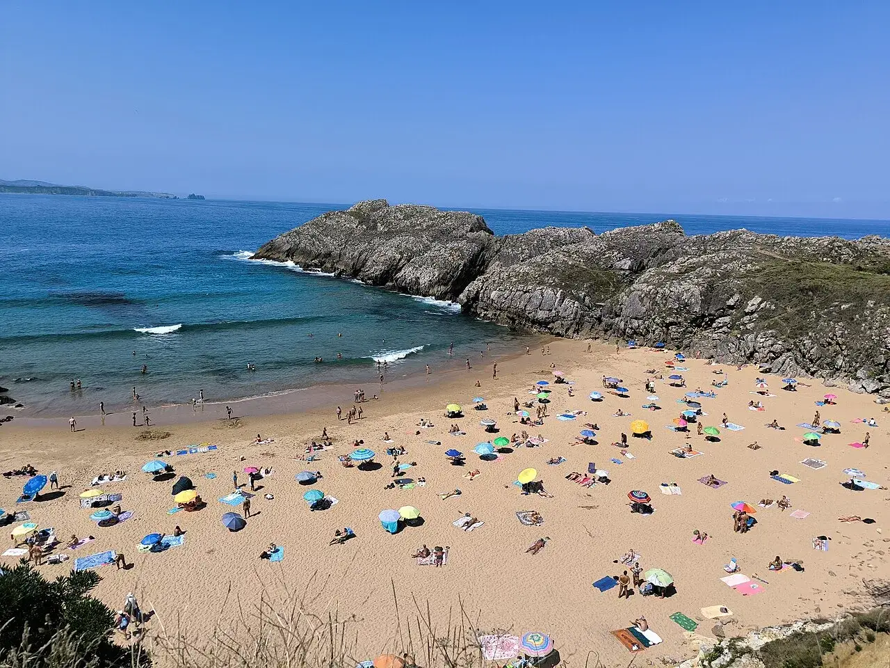 Gente disfrutando en la playa de Somocuevas, con sombrillas y el mar azul. Reseñas positivas para este paraíso.