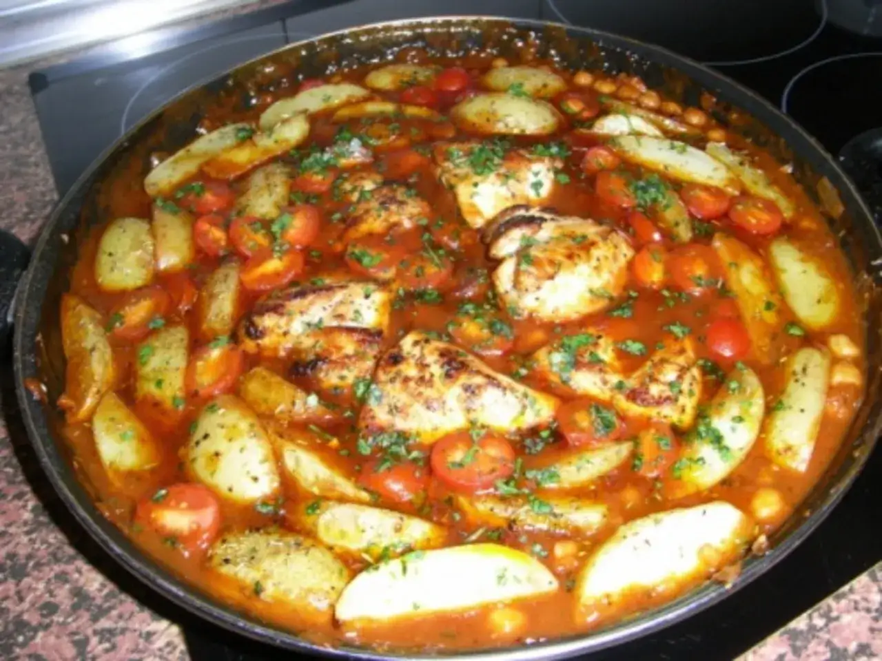 Herzhafter spanischer Eintopf mit H&auml;hnchen, Kartoffelspalten, Kirschtomaten und Kichererbsen in einer w&uuml;rzigen Tomatensauce, garniert mit Petersilie.