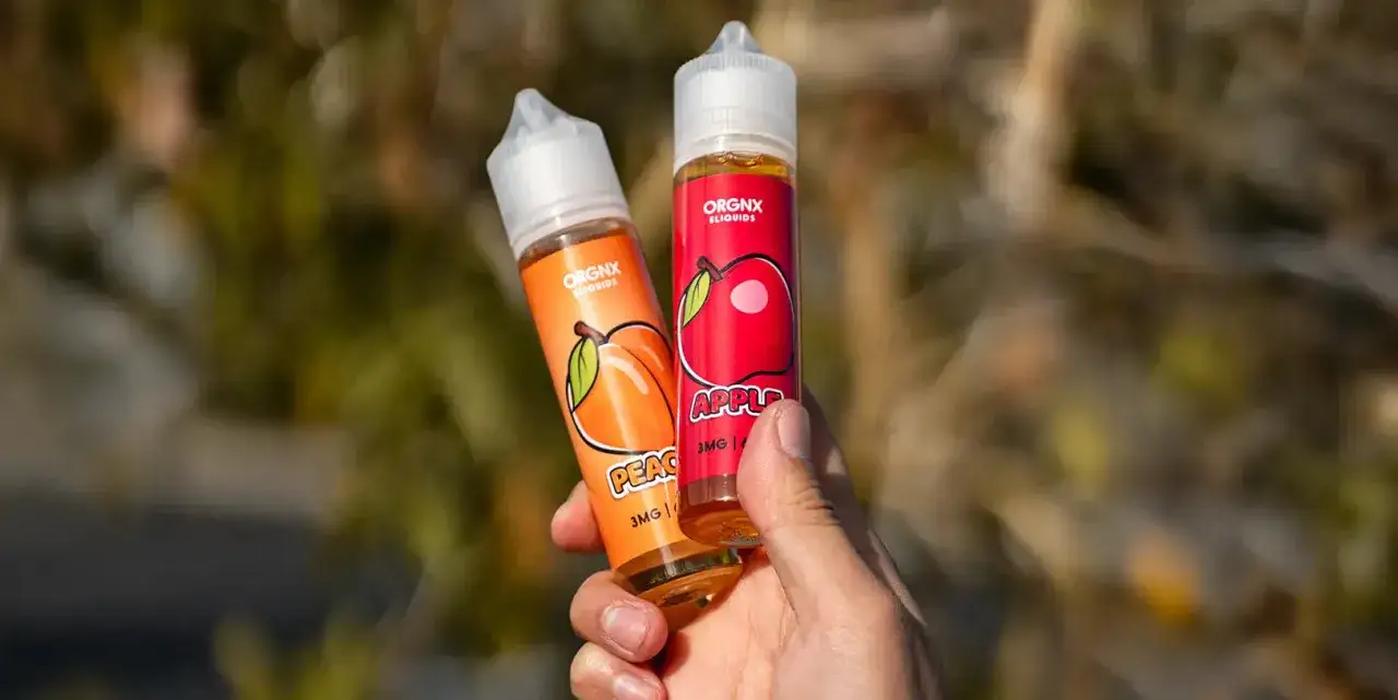 Dos botellas de drifter bar juice 100ml, una de melocotón y otra de manzana, sostenidas en una mano.