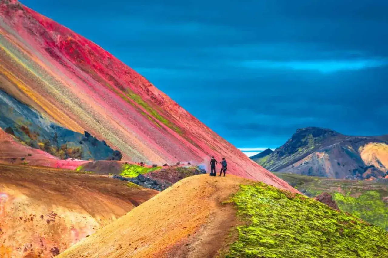 Deux randonneurs contemplent les montagnes multicolores de Landmannalaugar, un paysage spectaculaire pour un trek inoubliable.