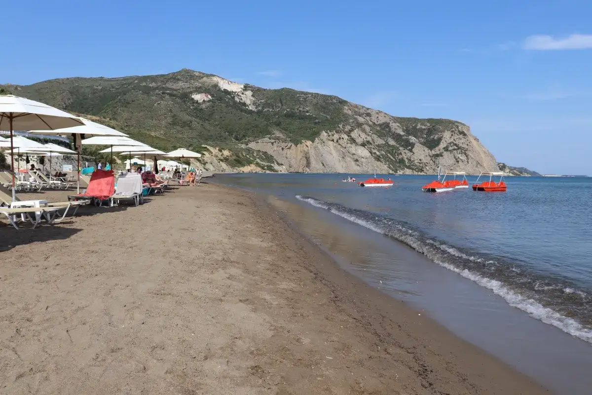 Piękna plaża Caretta z leżakami i parasolami, w tle góry i czerwone łódki na spokojnym morzu.
