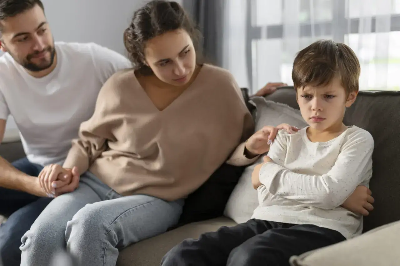 Genitori cercano di capire le emozioni dei bambini frasi, confortando il figlio pensieroso sul divano.