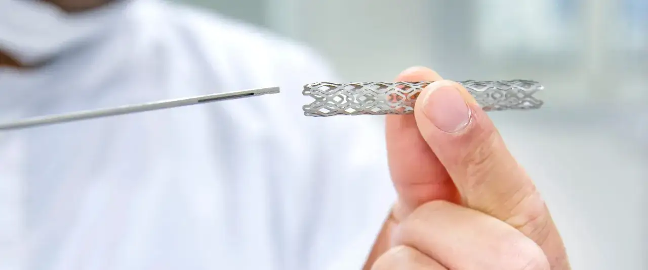 Dłoń trzyma metalowy stent, obok narzędzie medyczne. Badania nad tym, jak długo wytrzymują stenty, są kluczowe dla kardiologii.