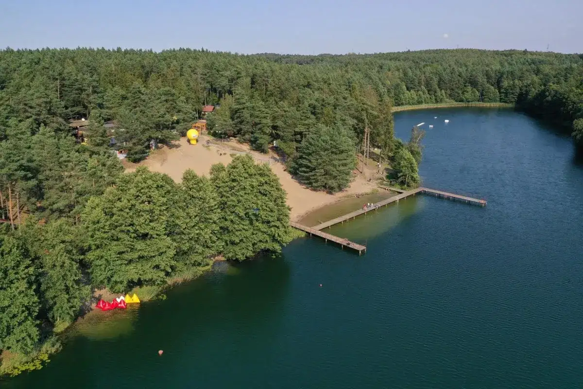 Malownicza borówno plaża z pomostem i kolorowymi łódkami, otoczona lasem. Idealne miejsce na letni wypoczynek.